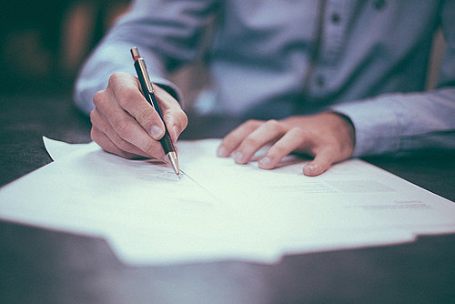 Fotografie einer Person, die mit einem Stift in ein Dokument schreibt.