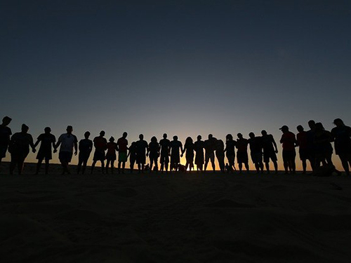 Große Gruppe junger Menschen, die aneinandergereiht im Sonnenuntergang stehen.