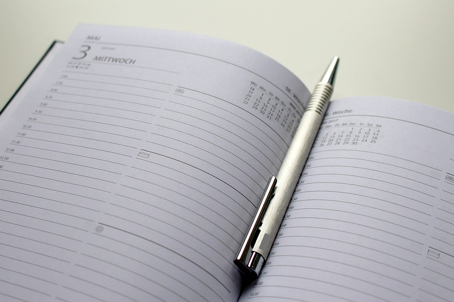 Fotografie eines aufgeschlagenen Terminplaners, in dessen Mitte ein silberner Kugelschreiber liegt